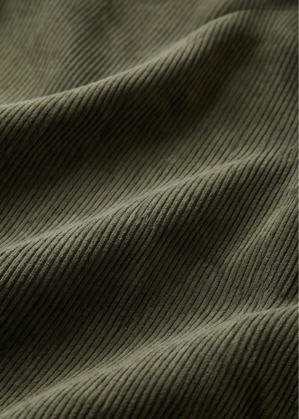 Close-up of olive green ribbed fabric with soft folds and a small warm beige patch visible near the lower left.