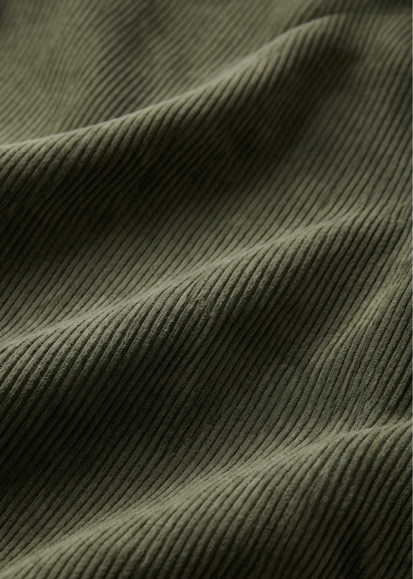 Close-up of olive green ribbed fabric with soft folds and a small warm beige patch visible near the lower left.