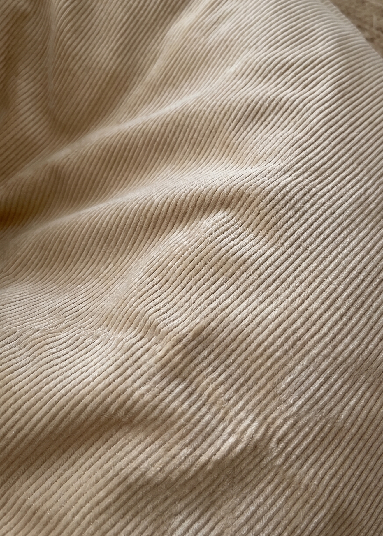A close-up of a beige corduroy fabric surface with visible ribbed texture, draped over a woven brown circular cushion or stool.