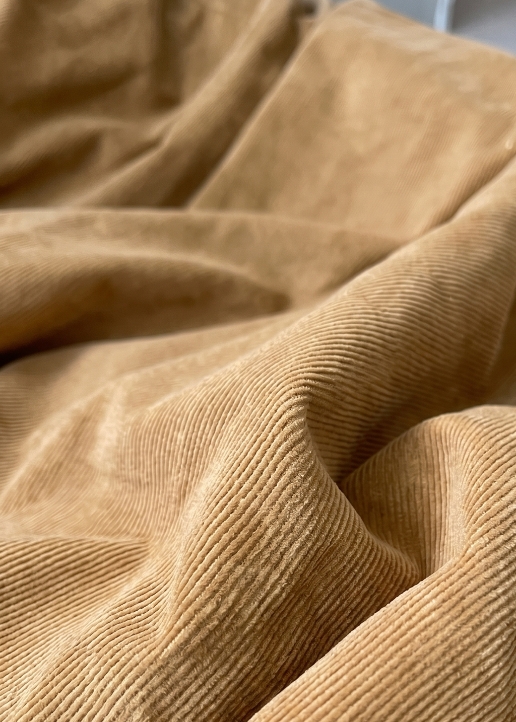 A close-up of draped tan corduroy fabric with a ribbed texture, filling the frame.