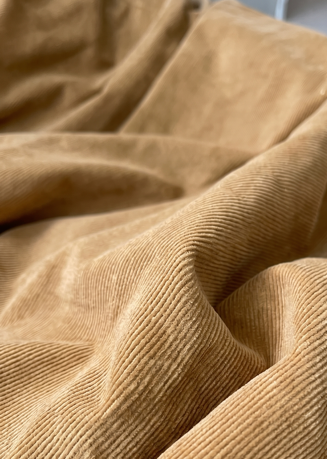 A close-up of draped tan corduroy fabric with a ribbed texture, filling the frame.