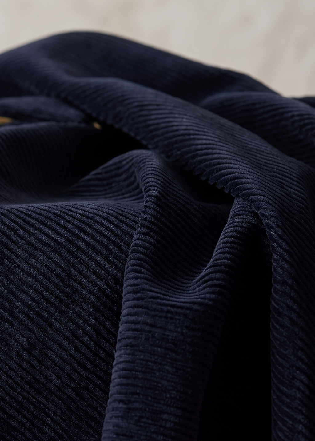 A close-up of dark navy blue corduroy fabric draped in soft folds, showing the ribbed texture and a small gold button detail.