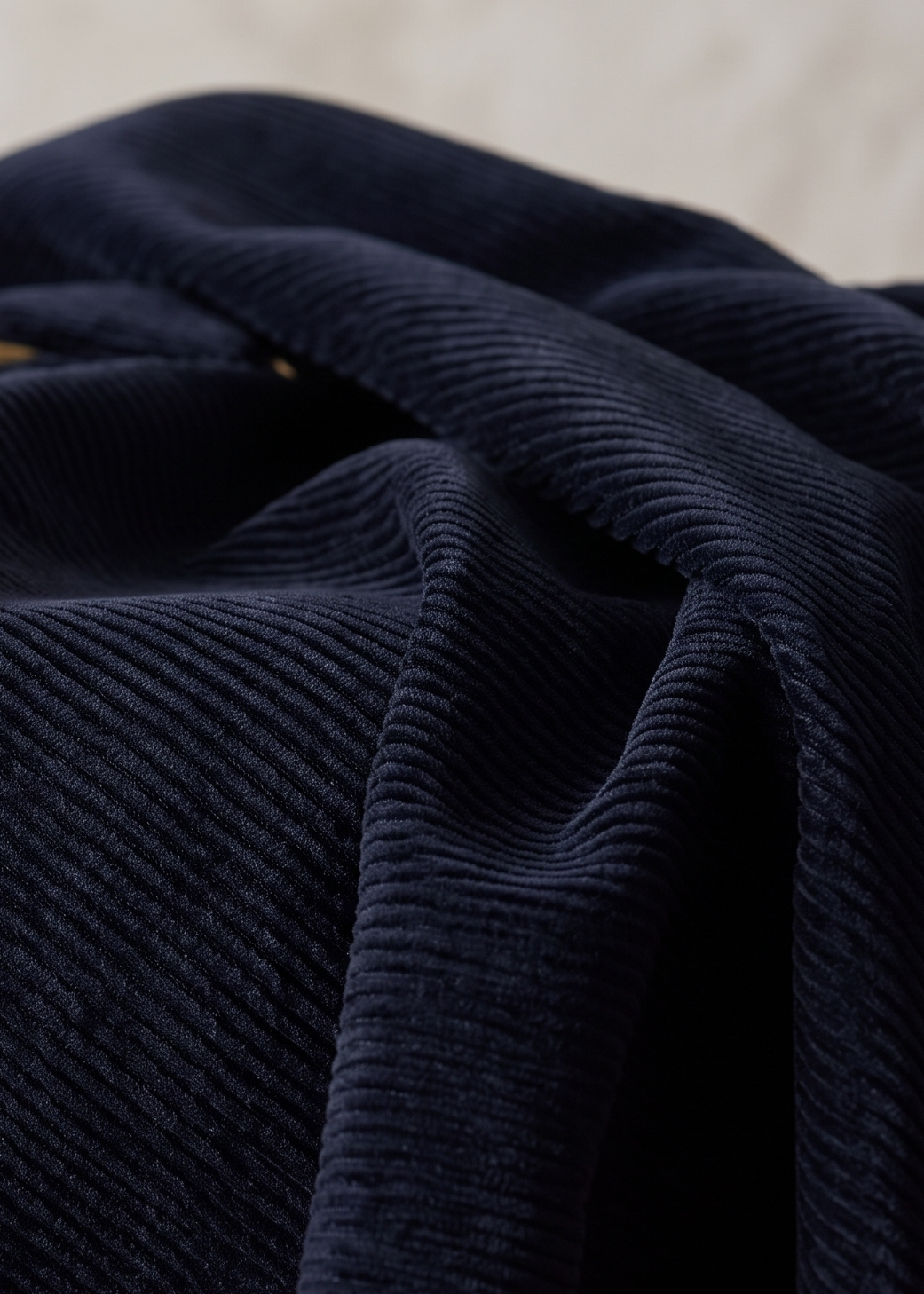 A close-up of dark navy blue corduroy fabric draped in soft folds, showing the ribbed texture and a small gold button detail.