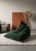 A dark forest green corduroy bean bag chair placed on a white shag rug in a modern minimalist living room setting.