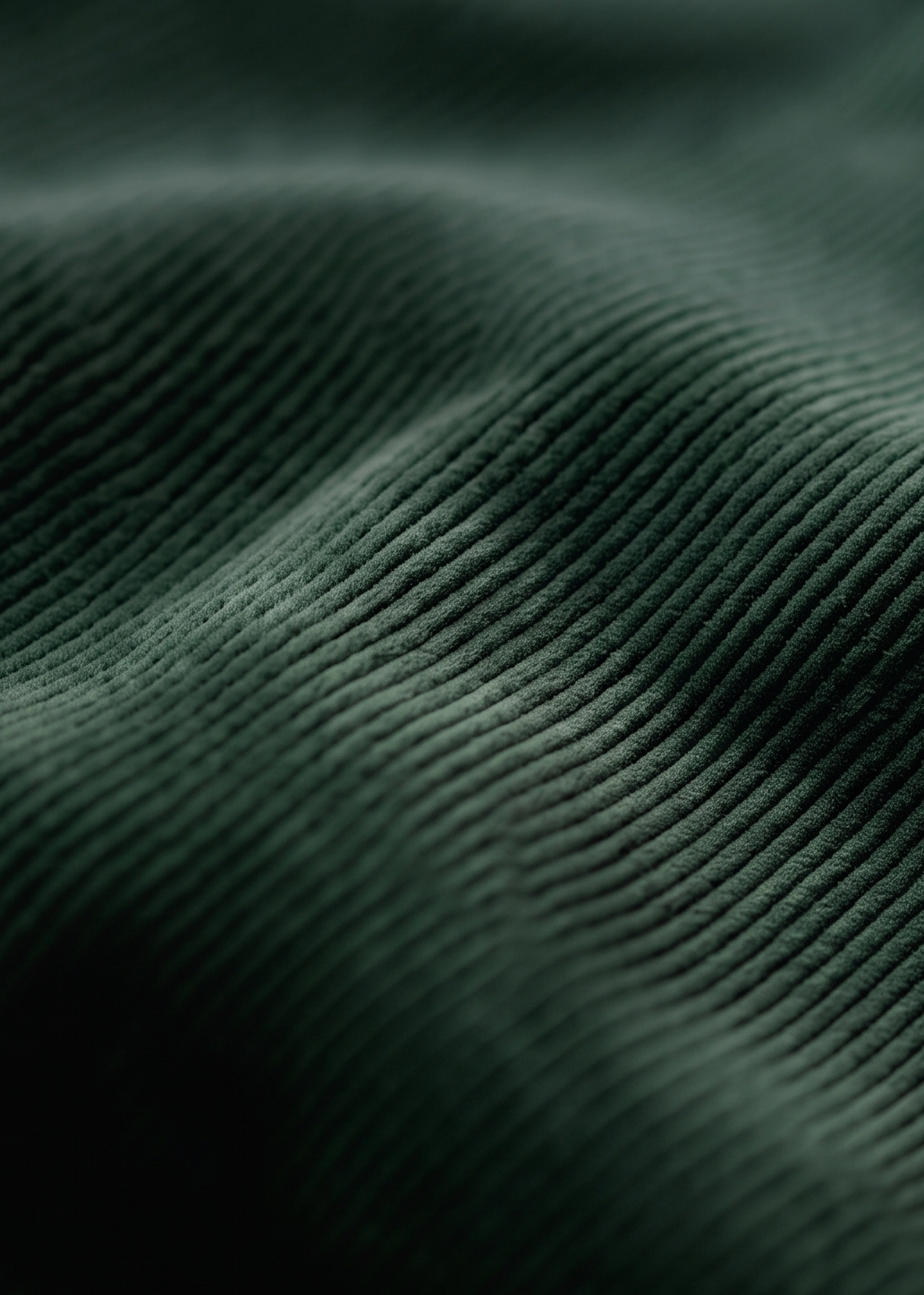 Close-up of dark forest green ribbed fabric texture with a soft peach-pink fabric partially visible along the right edge.